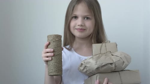 Young Girl Holding Gifts and Twine, Smiles