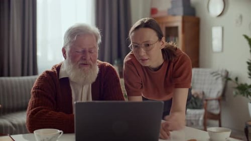 Woman Helping Senior Man Use Laptop at Home