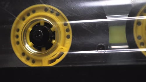 Yellow transparent audio cassette in the tape recorder. Playing and rotating. Close up, macro, side
