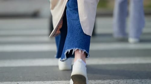 Closeup of Casual White Sneakers and Frayedhem Denim Stepping Across a City Crosswalk Capturing the