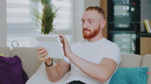 Man Relaxing on Sofa Video Calling on Tablet