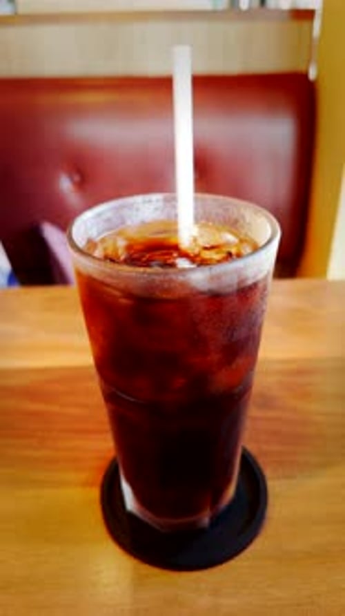 Vertical video. Close-Up Front View of a Hand Stirring Iced Cola with a Straw in a Frosted Glass on