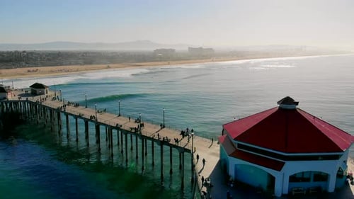 Fly in over Huntington Beach Pier and Diner toward shimmering sunrise on Pacific Ocean with Hilton &