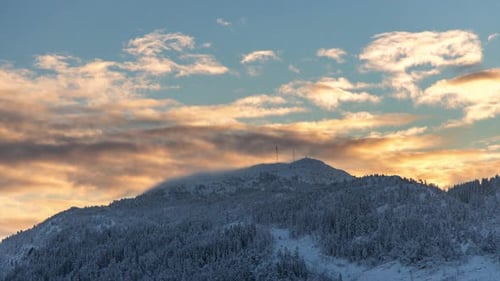 Goldene Wolken und Schneeschauer über dem Gipfel eines verschneiten Berges in Norwegen