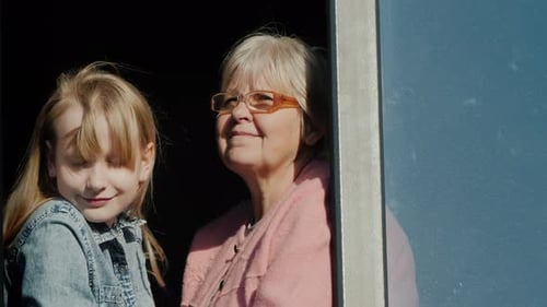 Senior Woman Next to the Child Sits on the Window Sill and Looks Out the Window Boring in Quarantine