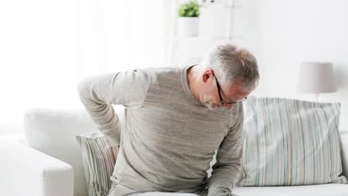 Mature man massaging lower back sitting on couch