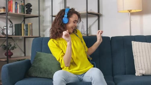 Cheerful Woman Dancing with Headphones on Sofa
