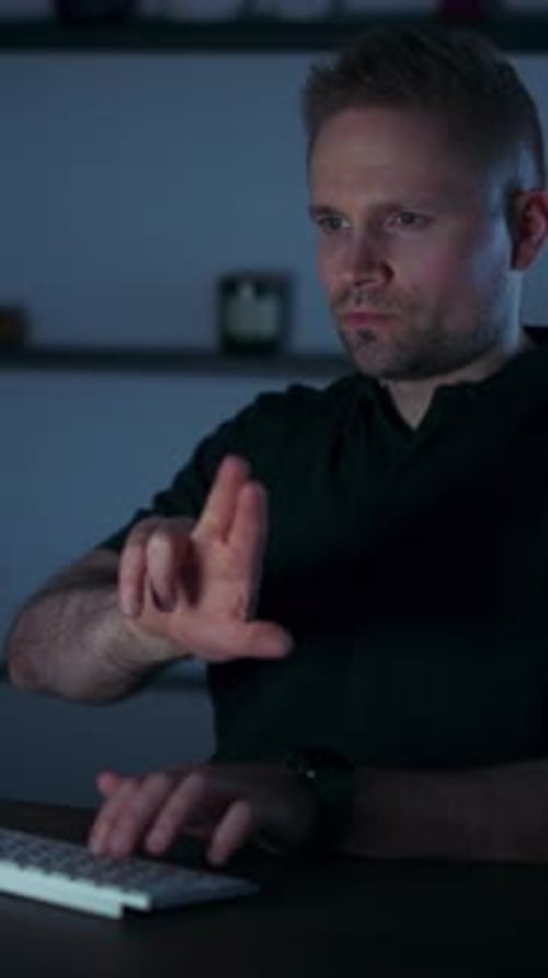 A Businessman in a Black Polo and Smartwatch Types in a Dim Office - Vertical Shot