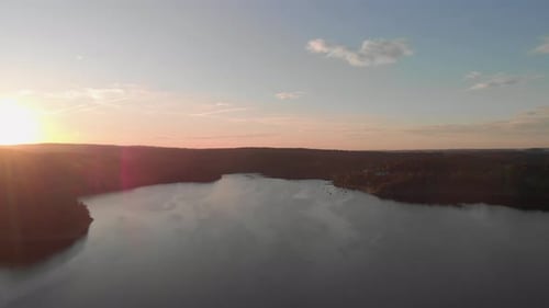 a professional looking aerial shot of a lake in pink orange sunset, flighing straight towards the su
