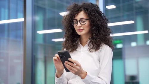 Businesswoman is using phone while standing at workplace in modern business office. Female manager