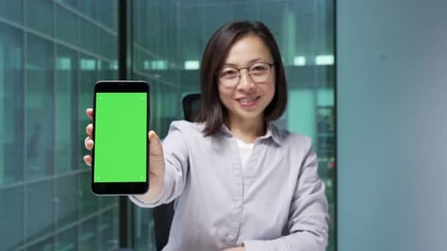 Happy asian businesswoman showing mobile phone with green screen in modern business office. Color