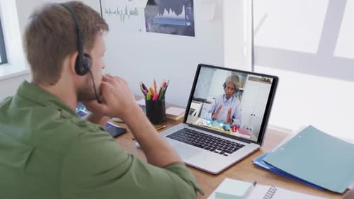 Caucasian man using laptop and phone headset on video call with female colleague