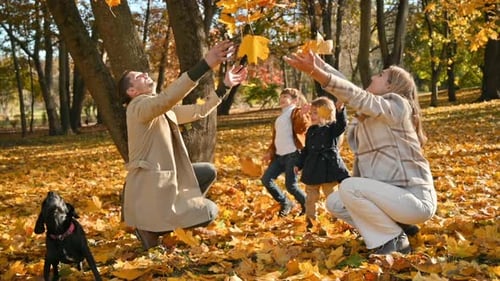 Happy family in an autumn park. Mother, father, daughter and son are throwing yellow leaves into the