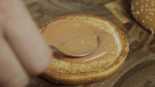 Adding homemade sauce onto burger bun. Close up shot. Slow motion