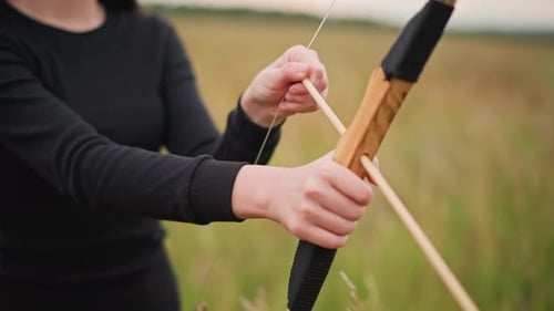 Young Woman Archer in Field Leatherwrapped Bow Gripped Steady Slow Draw Focused Gaze Tall Grass