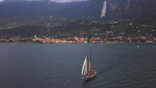 Segelschiff auf dem Gardasee mit den Klippen des Gardasees im Hintergrund an einem teilweise bewölkten Tag.