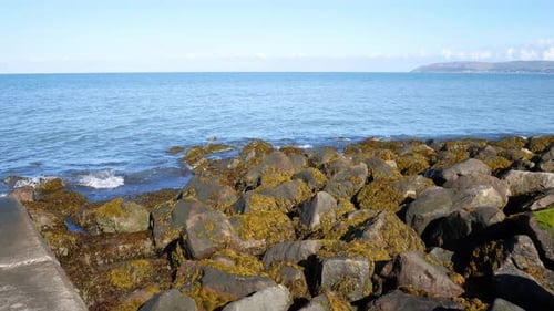 Sunny blue ocean stone pebble beach coastline island horizon holiday scene left dolly shot