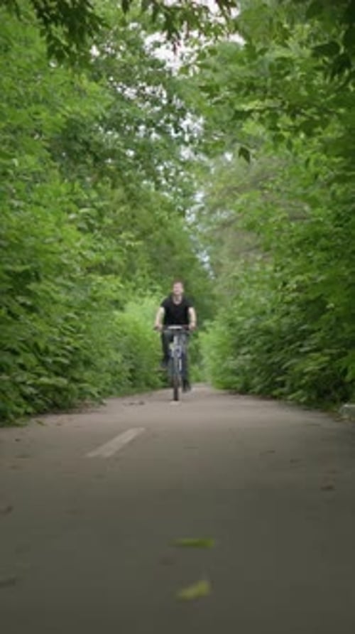 Young Boy Riding Bicycle Through Scenic Green Path Dodging Branches