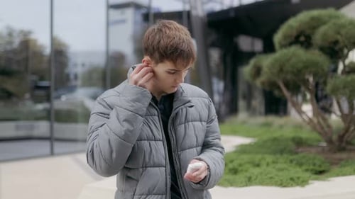 Teen Boy Takes Out Wireless Earbud While Enjoying a Peaceful Moment in the City