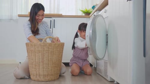 Asian beautiful mother teach young daughter wash dirty clothes at home.