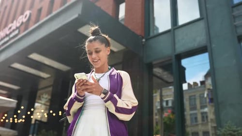 Woman Walking and Using a Smart Phone in the Street in a Sunny Summer Day