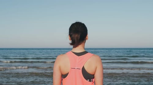 Back shot of female standing on the edge of coastline and looking at ocean horizon