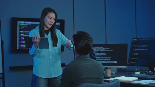 Asian woman holding digital tablet giving instructions to male programmer
