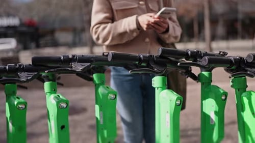 Woman Using Phone Near Row of Electric Scooters