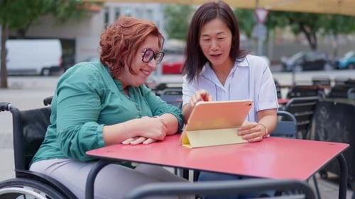 Two Women Enjoying Tablet at Outdoor Cafe