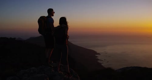 Couple, hiking and sunset for adventure, night and mountain top over ocean, standing and silhouette