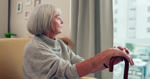 Senior Woman Sits Looking out Window with Cane
