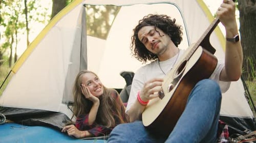 Man Plays Guitar for Woman Inside Camping Tent