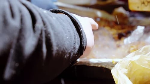 Gloved hand using tongs to grill food at a Christmas market with steam rising from sizzling meat