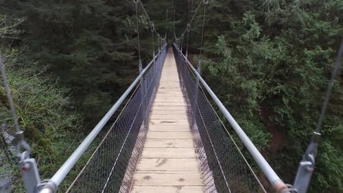 Walking Across A Narrow Suspension Bridge High Above Deep Forest