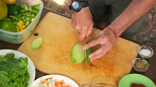 Vista superior de manos masculinas cortando vegetales verdes en una tabla de cortar mientras preparan la cena
