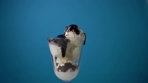 Sirope de chocolate vertido en crema batida cubierto de helado sobre fondo azul