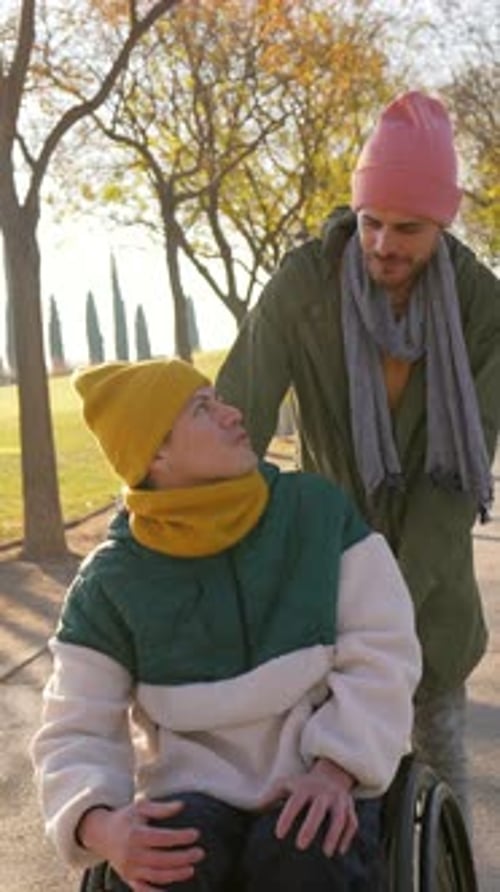 Young Man Pushing Friend in Wheelchair in a Park