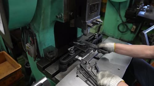 Worker pressing pliers blanks through mechanical stamping die on green industrial press