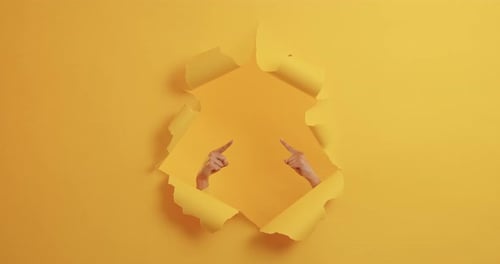Hands Pointing Upward Through a Torn Yellow Paper