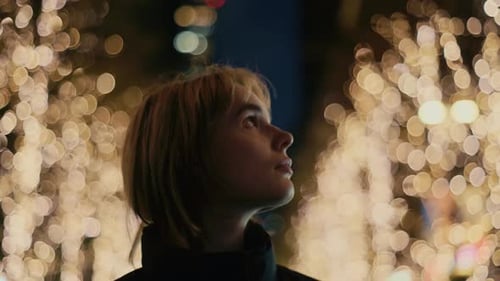 Young woman walking through city streets decorated with Christmas lights at night.