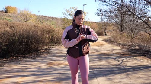 Female runner checking smartwatch while jogging on a sunny nature path in fall