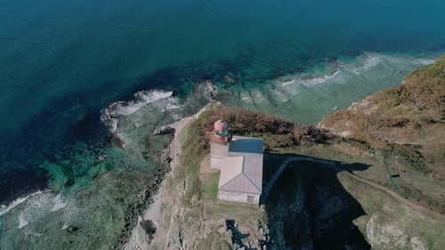 Panoramaaufnahme des weißen Leuchtturms auf der felsigen Klippe am Meer. Wellen stürzen auf den