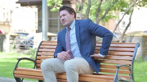 Man in Suit on Park Bench, Back Pain