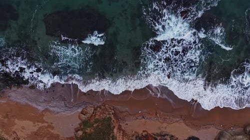 Bei hellem Tageslicht rollen Wellen auf einen Sandstrand in der Nähe von Felsformationen