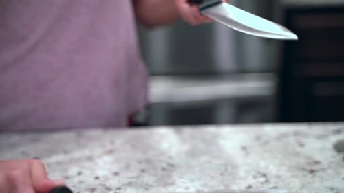 Close up of woman sharpening a knife over a countertop in slow motion