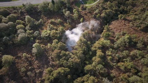 Aerial view circling around a natural hot spring within dense bushland and forest at golden hour