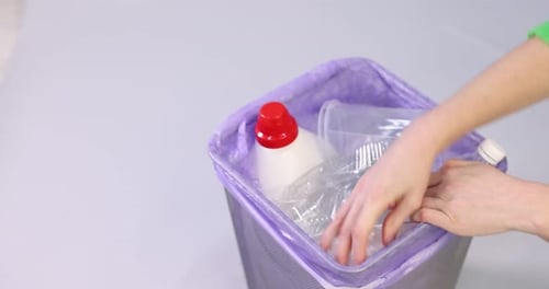 Hands filling a recycling bin with plastic waste