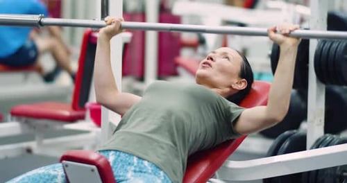 Middleaged Woman Performs Bench Presses in the Gym Focusing on Chest Muscle Strength