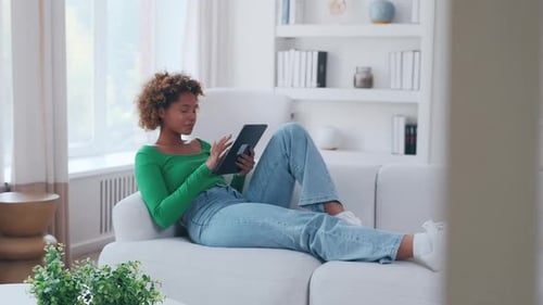 Woman Relaxes on Couch Using Tablet at Home
