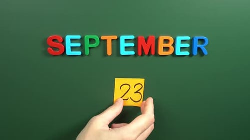 Hand sticking a sticker 23 September calendar day on school board. 23 date of September. Twenty